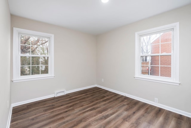 empty room with dark wood-type flooring, visible vents, plenty of natural light, and baseboards