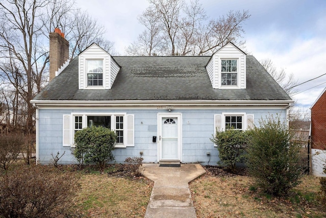 cape cod-style house with a chimney and roof with shingles