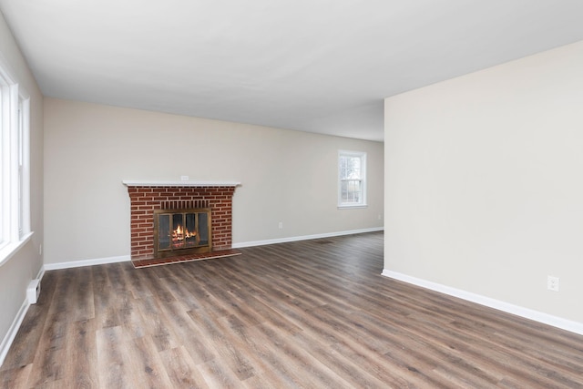 unfurnished living room featuring a brick fireplace, wood finished floors, and baseboards