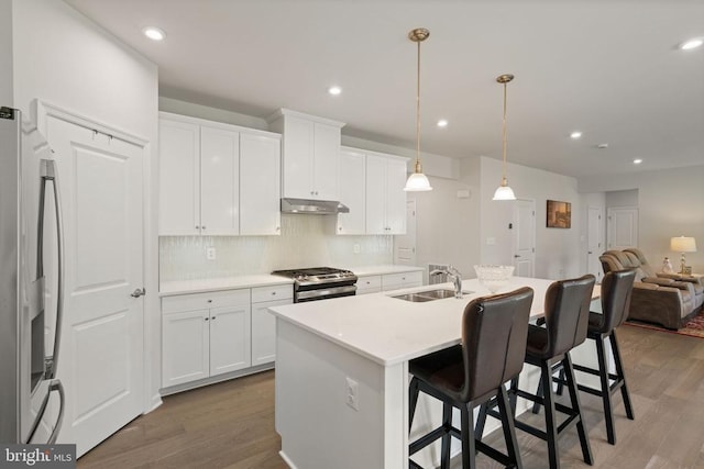 kitchen featuring appliances with stainless steel finishes, sink, white cabinets, hanging light fixtures, and a center island with sink