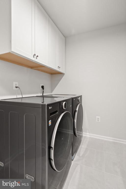 washroom with cabinets, light tile patterned floors, and washing machine and clothes dryer