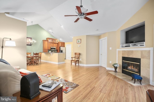 living room with baseboards, a tiled fireplace, vaulted ceiling, ceiling fan with notable chandelier, and light wood-style floors