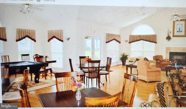 dining space featuring a glass covered fireplace, high vaulted ceiling, wood finished floors, and ceiling fan