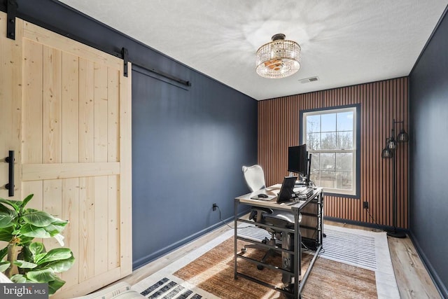 home office featuring a barn door, light wood-style flooring, visible vents, and baseboards