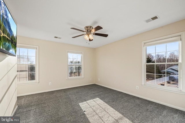 spare room featuring dark colored carpet, plenty of natural light, and visible vents