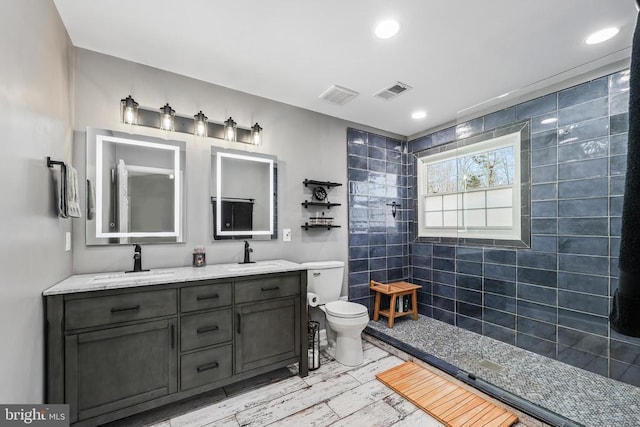 bathroom featuring visible vents, a sink, toilet, and tiled shower