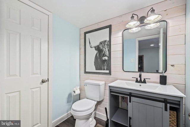 bathroom featuring toilet, wood walls, wood finished floors, vanity, and baseboards