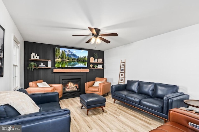 living area featuring light wood-style floors, a glass covered fireplace, and ceiling fan