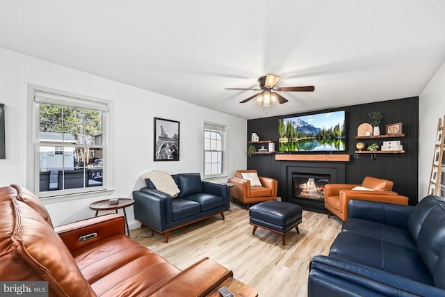 living room featuring light wood finished floors, a glass covered fireplace, and a ceiling fan