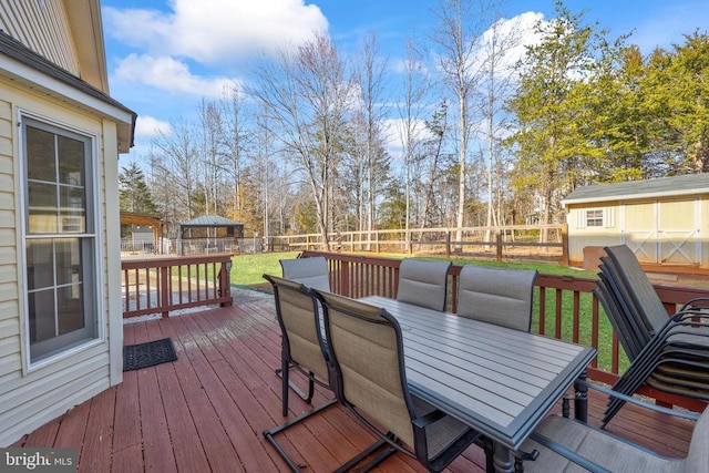 wooden deck with a yard, outdoor dining area, an outdoor structure, and a fenced backyard