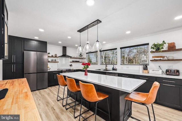 kitchen with appliances with stainless steel finishes, dark cabinetry, wall chimney exhaust hood, and open shelves