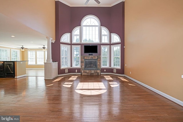 unfurnished living room with decorative columns, wood-type flooring, a stone fireplace, and a ceiling fan