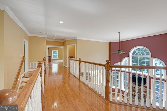 hallway featuring hardwood / wood-style floors, visible vents, baseboards, crown molding, and an upstairs landing