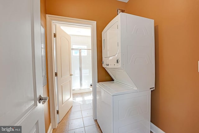 clothes washing area featuring baseboards, light tile patterned flooring, laundry area, and stacked washing maching and dryer