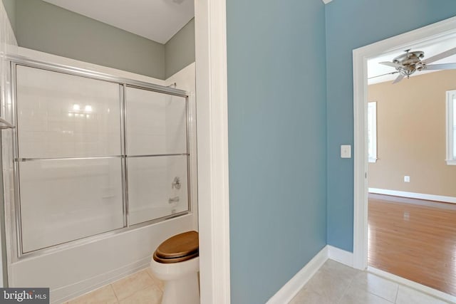 bathroom with tile patterned floors, baseboards, toilet, and bath / shower combo with glass door