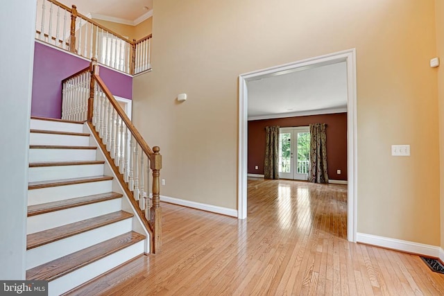 stairway featuring baseboards, a high ceiling, ornamental molding, french doors, and wood-type flooring