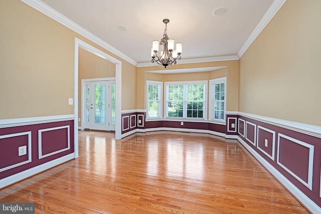 spare room with a wainscoted wall, light wood finished floors, an inviting chandelier, ornamental molding, and a decorative wall