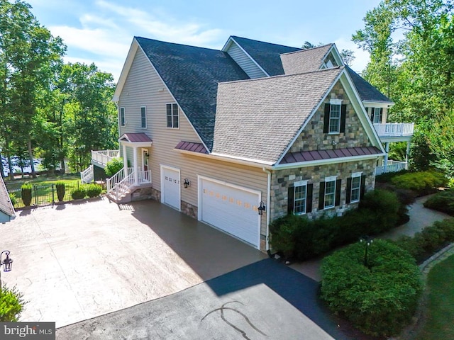 view of front of house featuring a standing seam roof, stone siding, concrete driveway, an attached garage, and a balcony