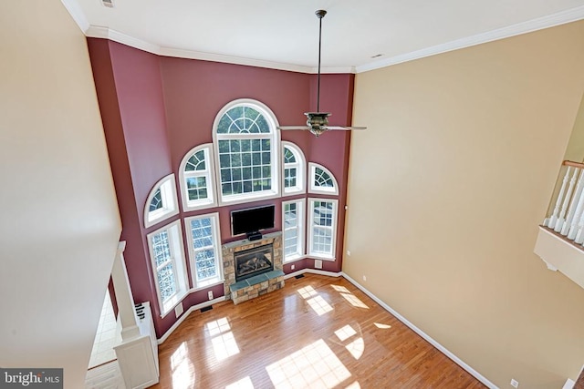 living area featuring a ceiling fan, wood finished floors, a fireplace, crown molding, and baseboards