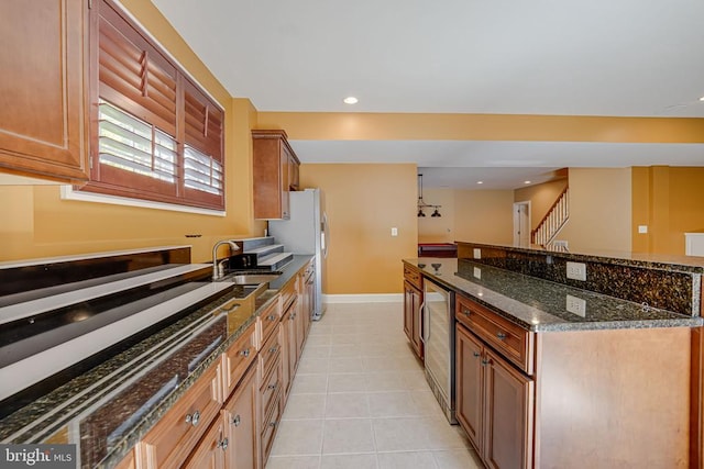 kitchen featuring a sink, dark stone countertops, wine cooler, light tile patterned floors, and baseboards