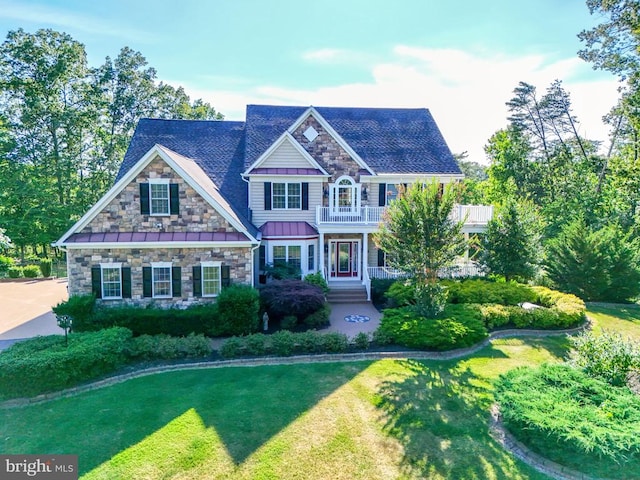 view of front of house featuring a standing seam roof, stone siding, a front lawn, and a balcony