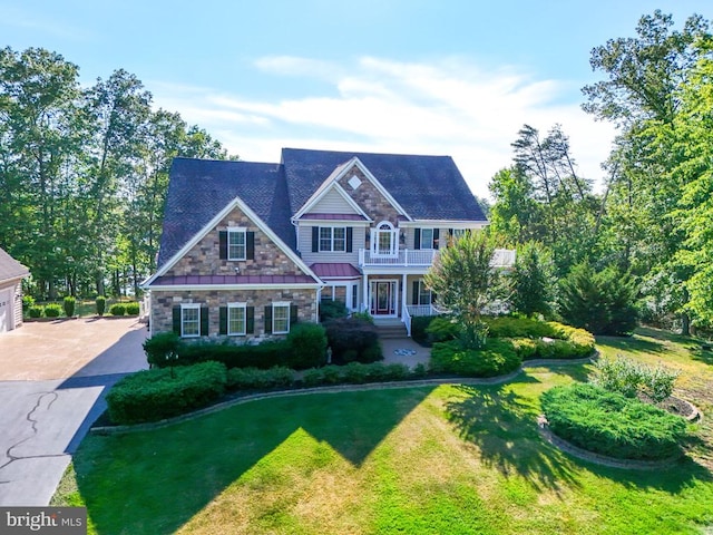 view of front of house featuring a standing seam roof, stone siding, a front yard, a garage, and a balcony