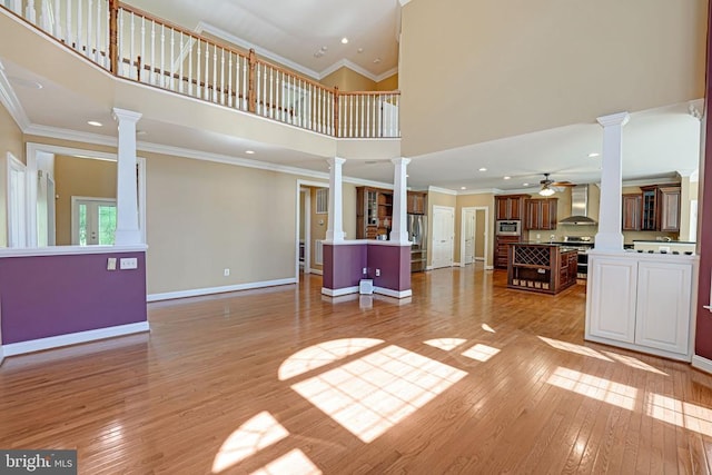 unfurnished living room with light wood finished floors, ceiling fan, crown molding, and ornate columns