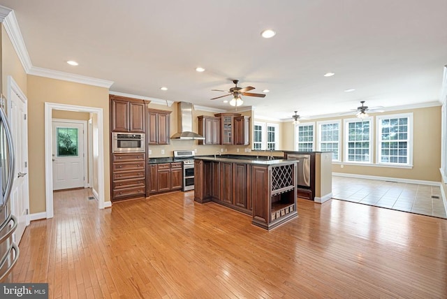 kitchen featuring dark countertops, light wood finished floors, crown molding, appliances with stainless steel finishes, and wall chimney exhaust hood