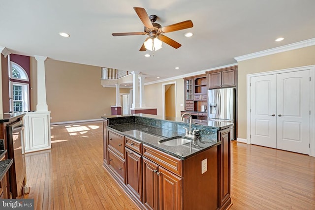 kitchen with decorative columns, an island with sink, stainless steel fridge, and a sink