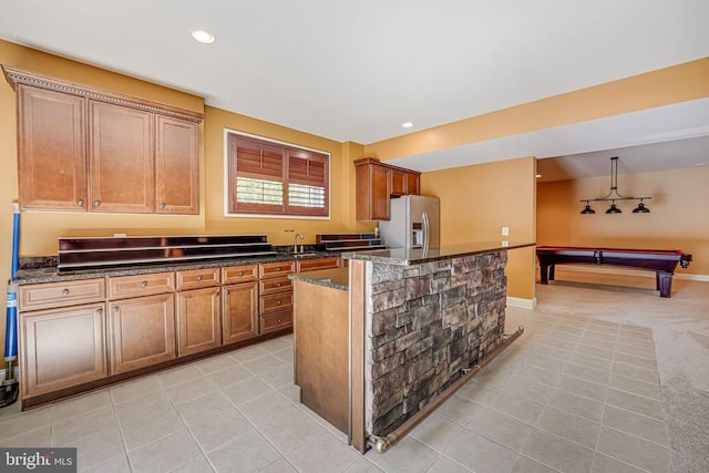 kitchen featuring dark stone countertops, light tile patterned floors, a kitchen island, a sink, and stainless steel fridge