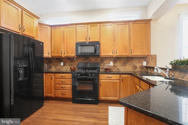 kitchen with sink, light hardwood / wood-style flooring, kitchen peninsula, dark stone counters, and black appliances