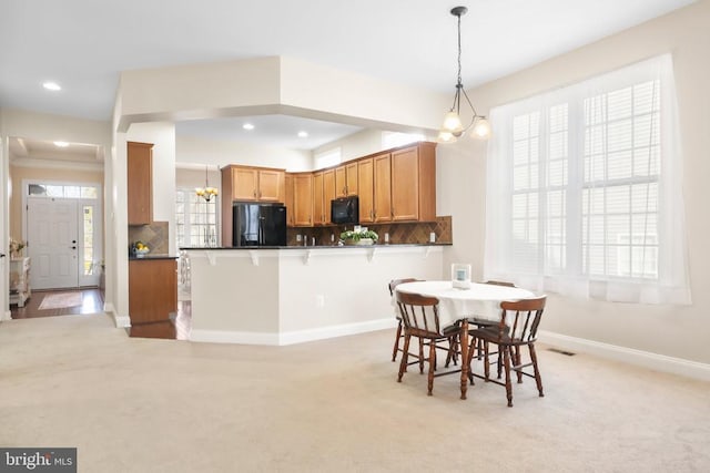 kitchen featuring pendant lighting, a breakfast bar area, black appliances, decorative backsplash, and kitchen peninsula