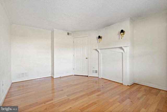 empty room with ornamental molding, a textured ceiling, and light hardwood / wood-style floors