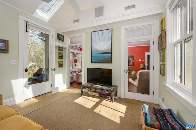 carpeted living area with vaulted ceiling with skylight, visible vents, and baseboards