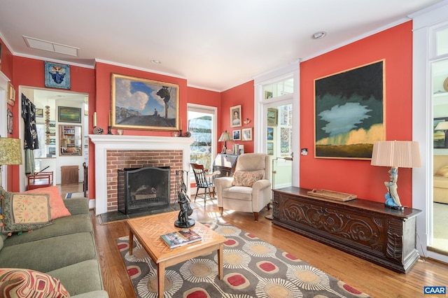 living room with a brick fireplace, visible vents, ornamental molding, and wood finished floors