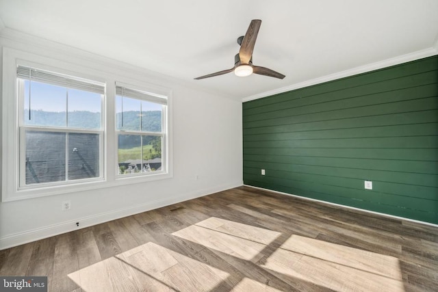 unfurnished room with crown molding, ceiling fan, wood walls, and hardwood / wood-style flooring