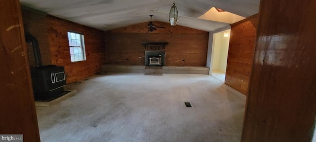 unfurnished living room with vaulted ceiling, a wood stove, wood walls, and ceiling fan