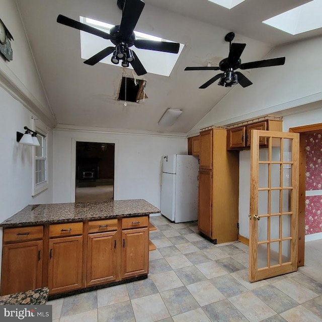 kitchen with lofted ceiling with skylight, brown cabinets, freestanding refrigerator, and a ceiling fan