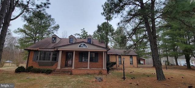 view of front of house featuring brick siding, covered porch, cooling unit, and a front lawn