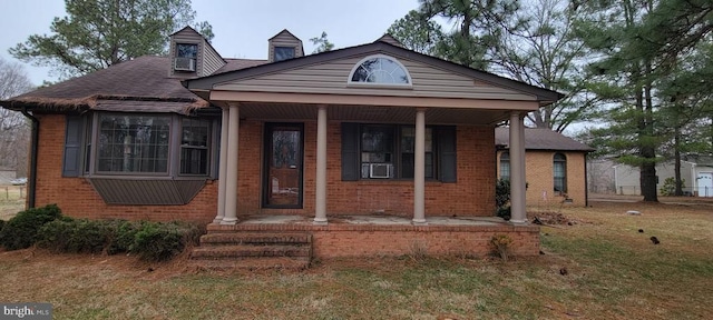 view of front facade featuring a front yard, a porch, brick siding, and a shingled roof