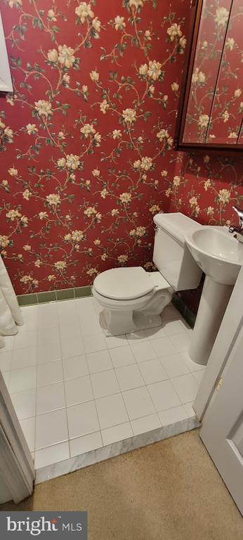 bathroom with toilet, wallpapered walls, and baseboards