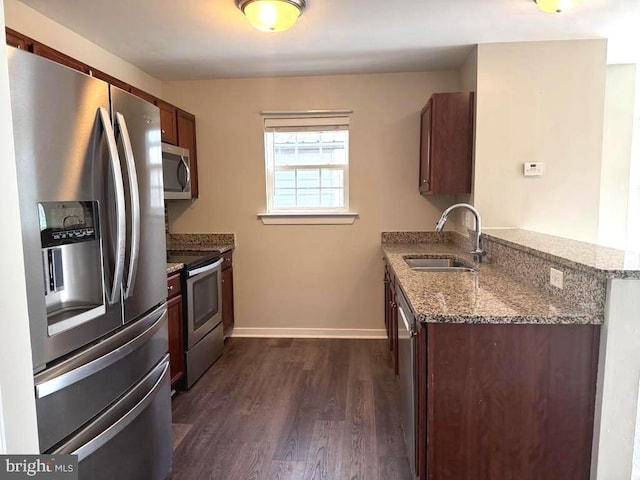 kitchen with a sink, dark stone countertops, stainless steel appliances, a peninsula, and dark wood-style flooring