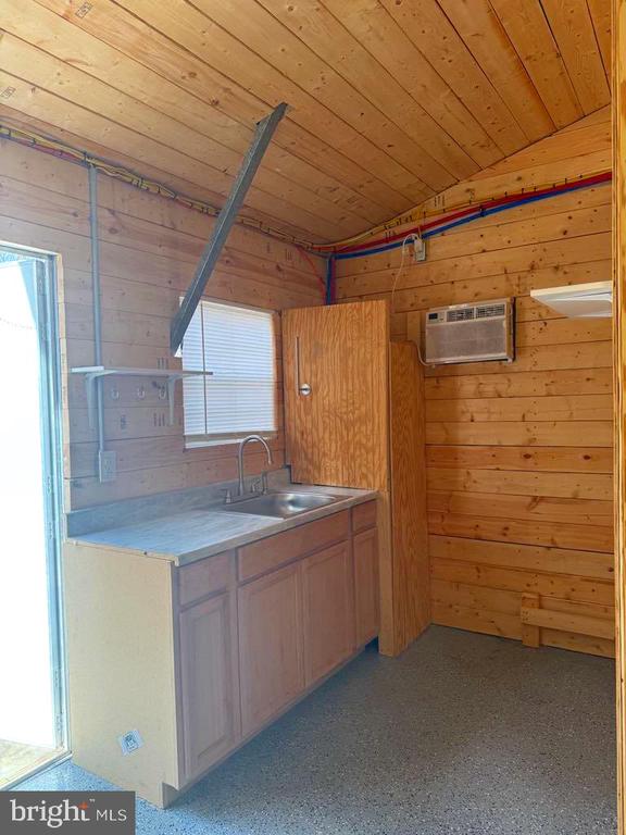 kitchen featuring wooden walls, a wall mounted air conditioner, wood ceiling, light countertops, and a sink