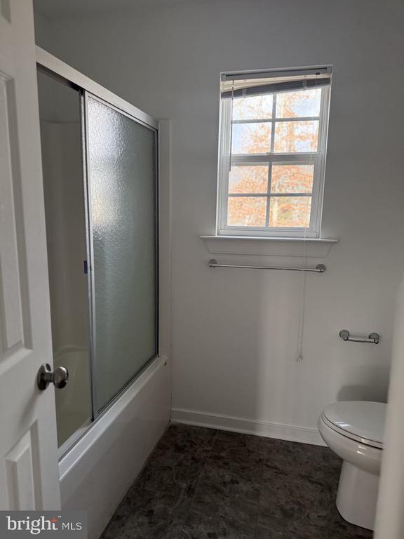 bathroom with toilet and bath / shower combo with glass door