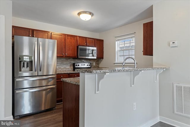 kitchen with visible vents, decorative backsplash, appliances with stainless steel finishes, a peninsula, and a kitchen breakfast bar