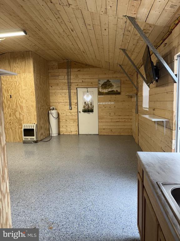 interior space featuring heating unit, wooden walls, wooden ceiling, speckled floor, and vaulted ceiling