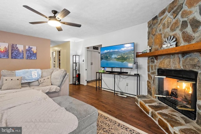 living room featuring dark hardwood / wood-style flooring, a stone fireplace, and ceiling fan