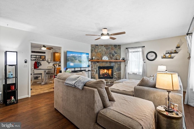 living room featuring a stone fireplace, dark wood-type flooring, a textured ceiling, and ceiling fan