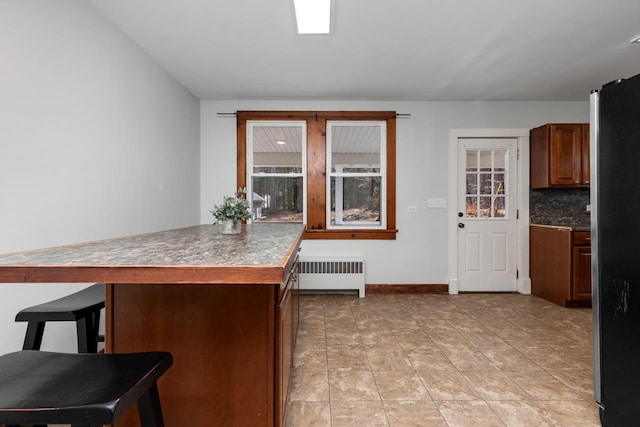 kitchen featuring radiator heating unit, stainless steel refrigerator, backsplash, a kitchen bar, and kitchen peninsula