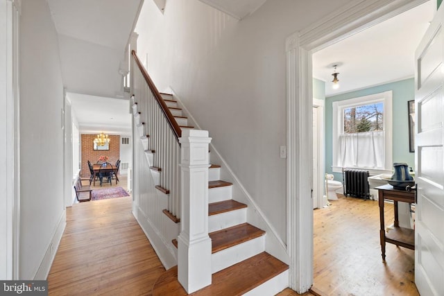 stairway with radiator heating unit, a chandelier, and wood-type flooring